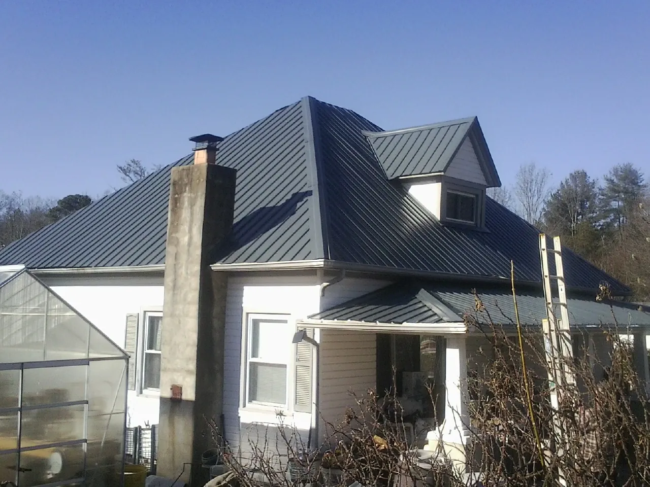 Dark blue standing seam metal roof on a white farmhouse with dormer — Slate & Tile Roof Repair by Roofing Brothers in Algona