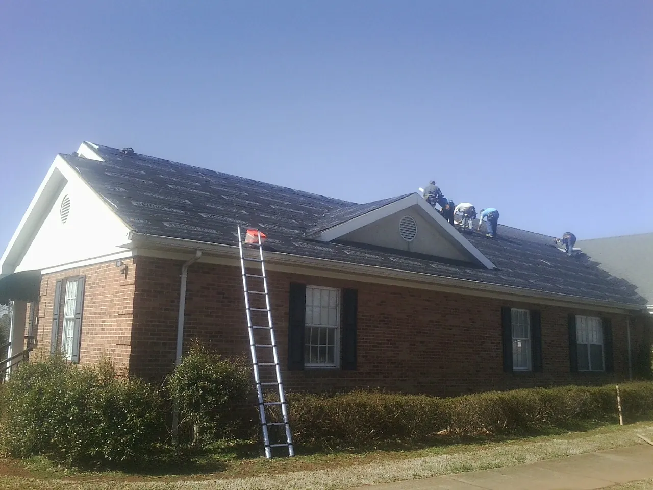 Crew tearing shingles off a brick ranch roof with a ladder set — Metal Roof Repair work by our crew in Algona