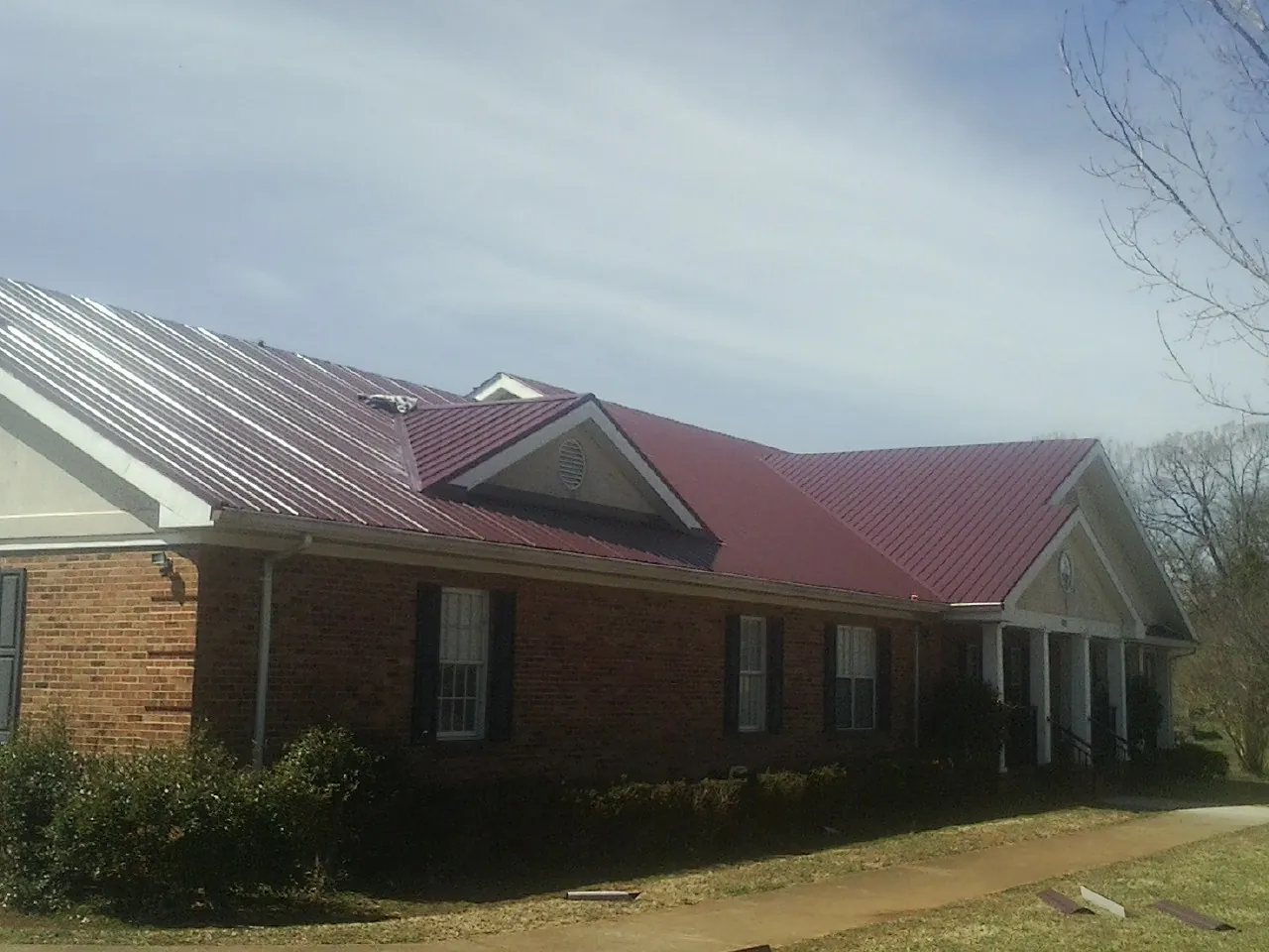Red metal roof with gabled entries on a long brick building, from a Hail Damage Roof Repair job in Algona