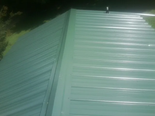 New green metal panels meeting at the ridge of a roof — Flat Roof Repair work by our crew in Algona