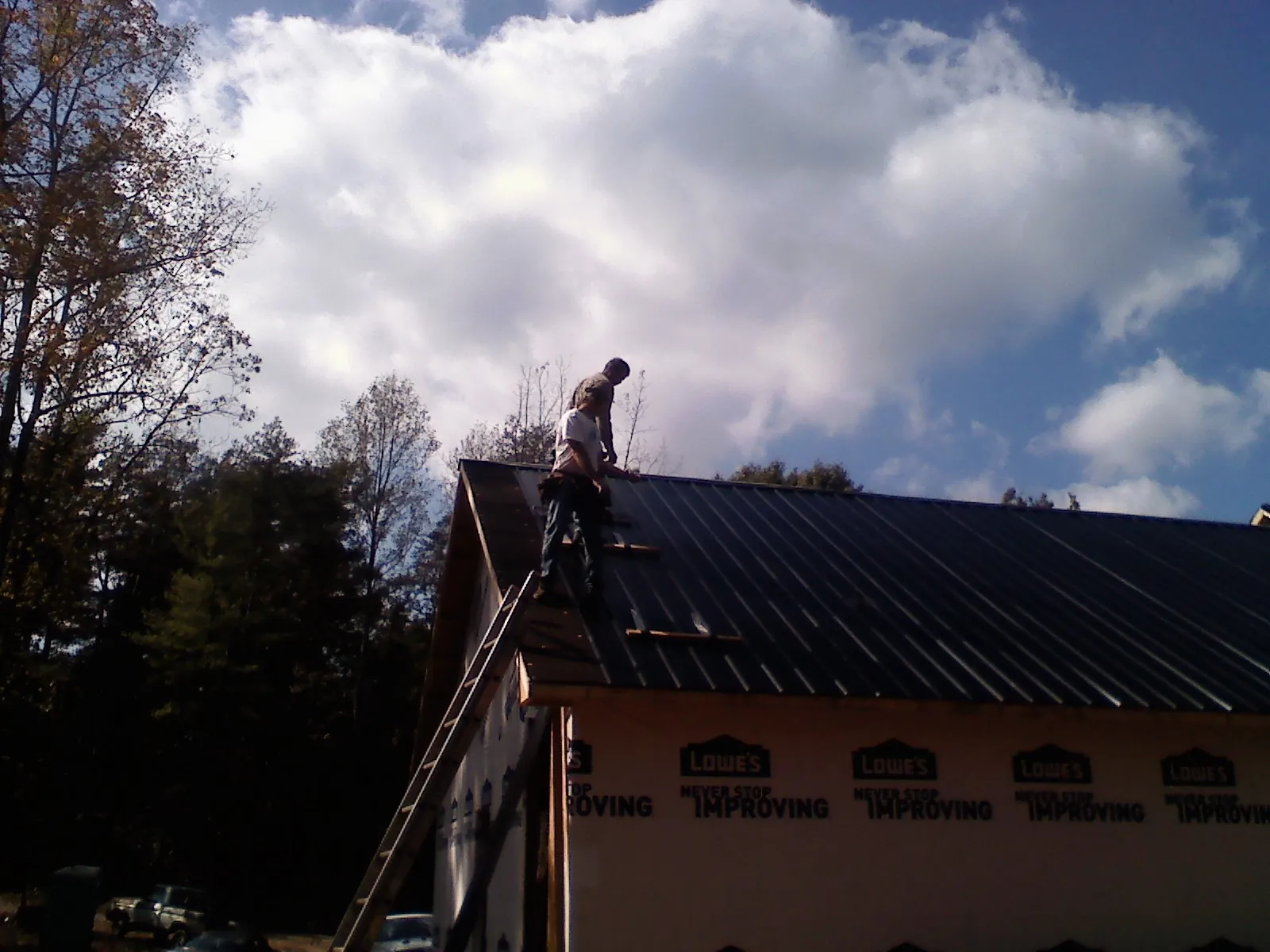 Roofer fastening dark metal panels high against a cloudy sky, from a Roof Inspection job in Algona