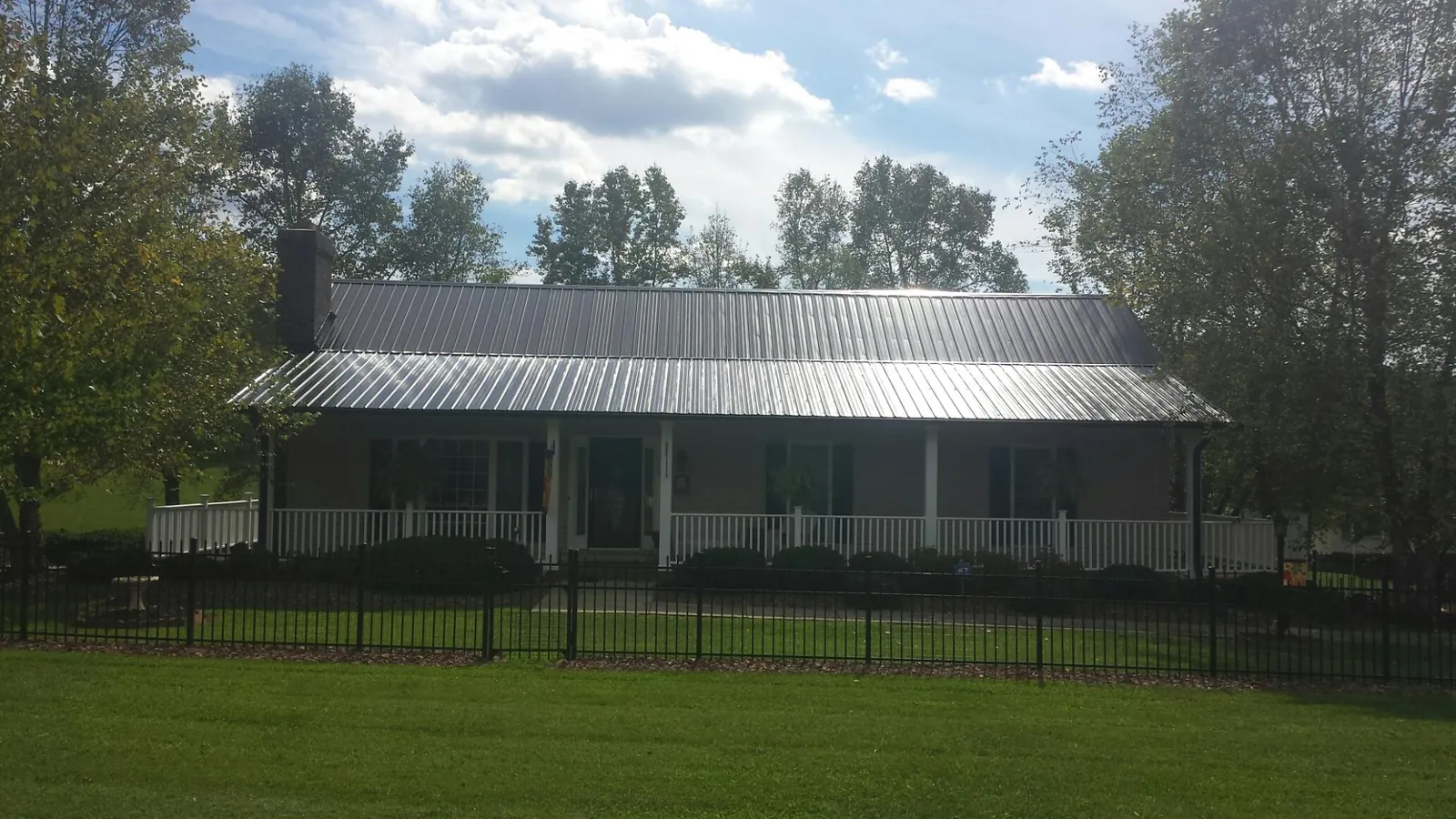 Gray metal roof on a brick ranch with a full width front porch — Gutter Guard Installation work by our crew in Algona