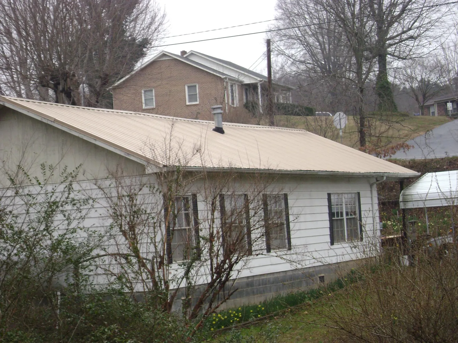Tan metal roof on a white sided house set into a hillside — Commercial Roofing by Roofing Brothers in Algona